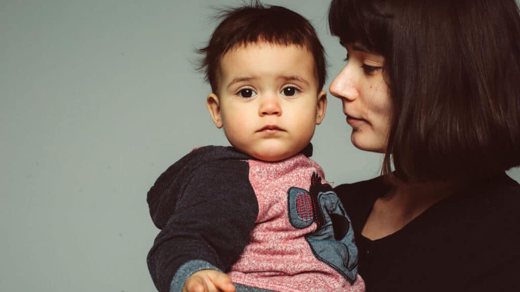 A woman with dark hair holds her baby, who is looking at the camera.