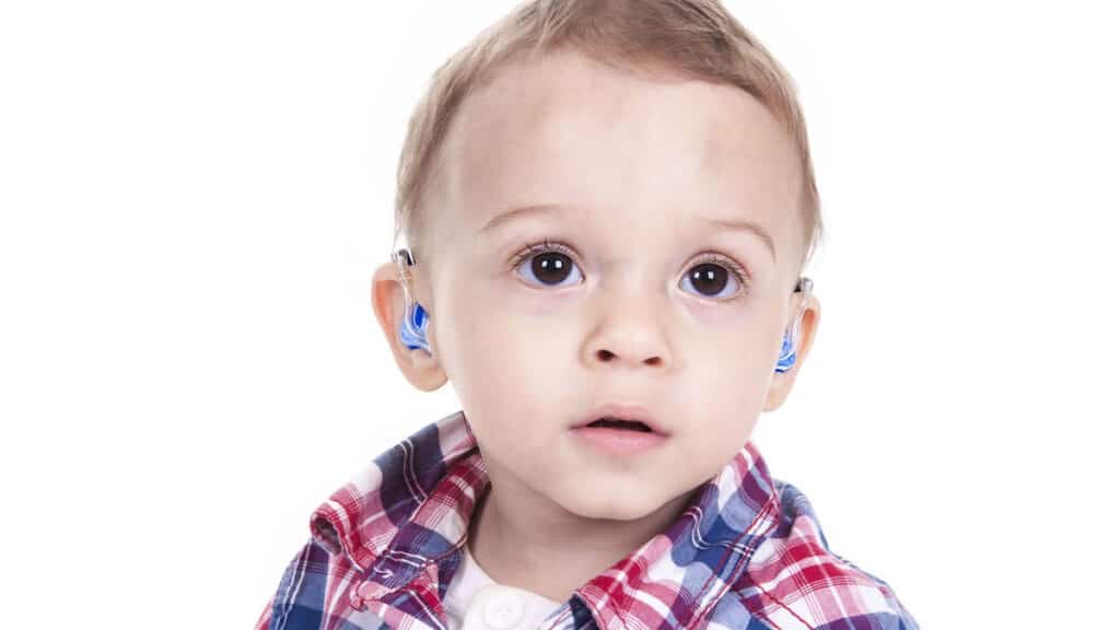 A toddler with big brown eyes and blue hearing aids.