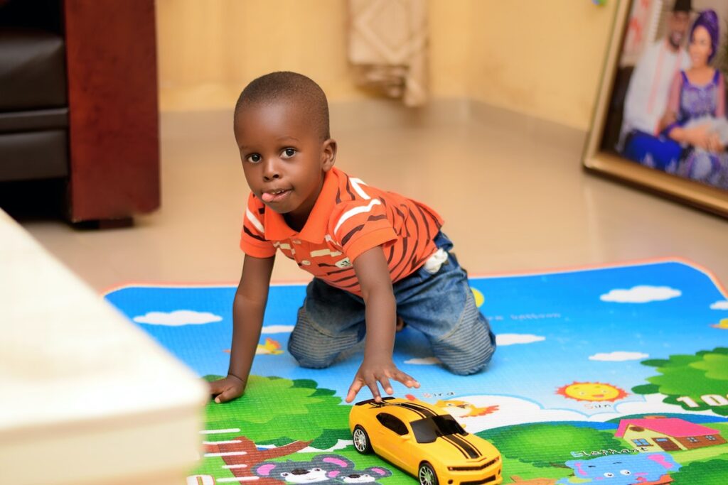 A small boy kneels on a colorful mat and pushes a toy car. Photo by Segun Osunyomi on Unsplash