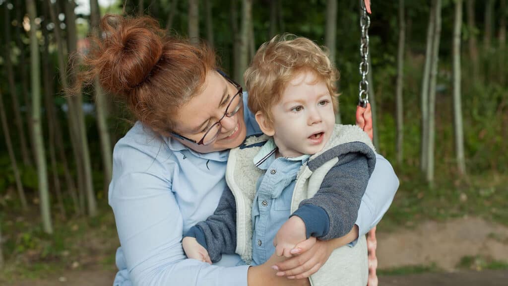 A woman holds her young son on a swing. She can be the rep payee for his SSI benefits.