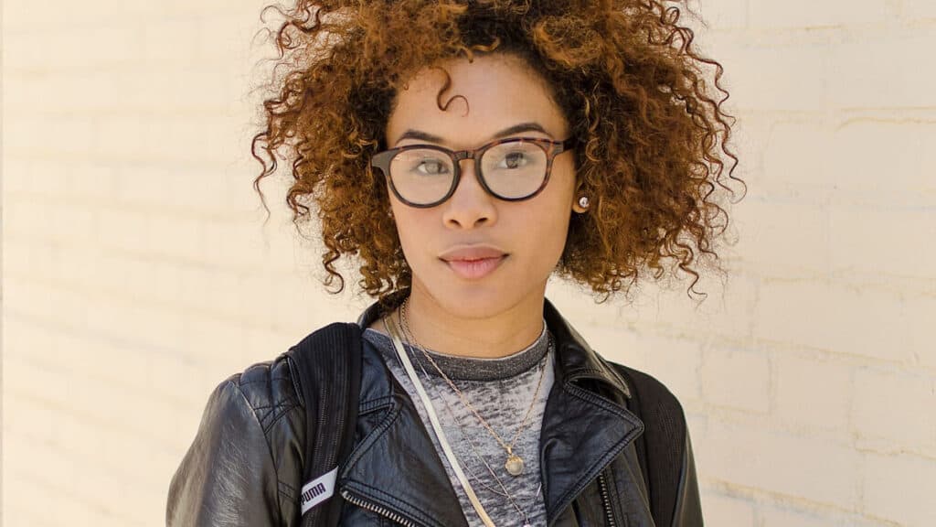 A student with brown curly hair and glasses looks directly at the camera.