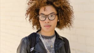 A student with brown curly hair and glasses looks directly at the camera.