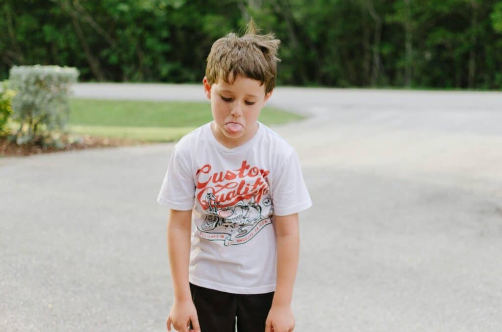 A boy is standing slumped with his tongue out, looking frustrated. Photo by Hunter Johnson on Unsplash