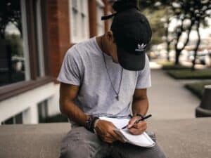 High school student struggles with homework. He is sitting on a bench outside of his school.