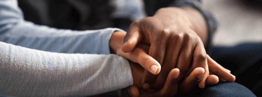 [Image Description: Three hands holding on the one another. The hand and arm furthest to the right is brown wearing a heather grey long sleeve shirt. The hand and arm in the middle is light brown wearing a light blue long sleeve shirt. The hand and …