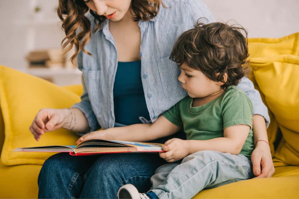 A mother reads to her toddler on the couch.
