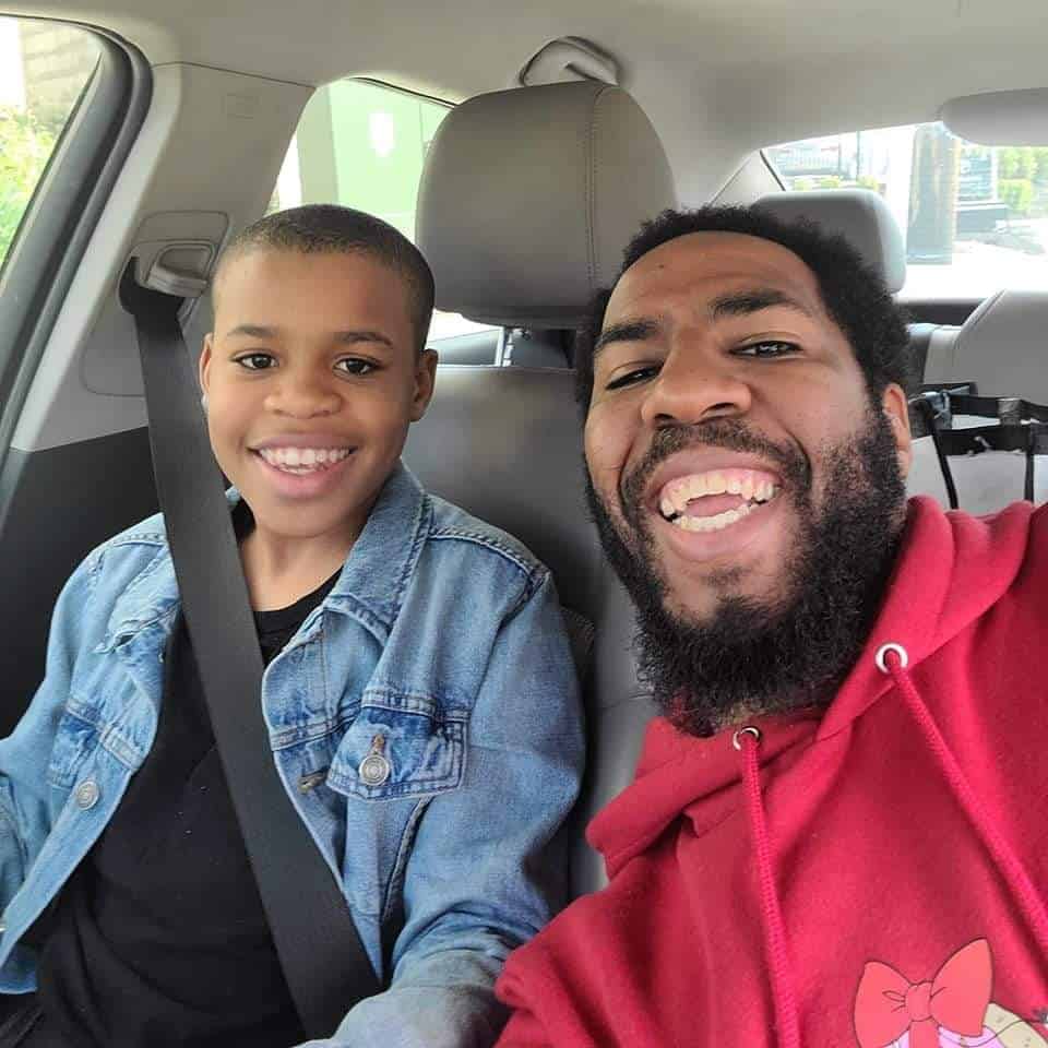 Maurice, a Black man sitting in the car smiling with Maurice Jr.., his Black son