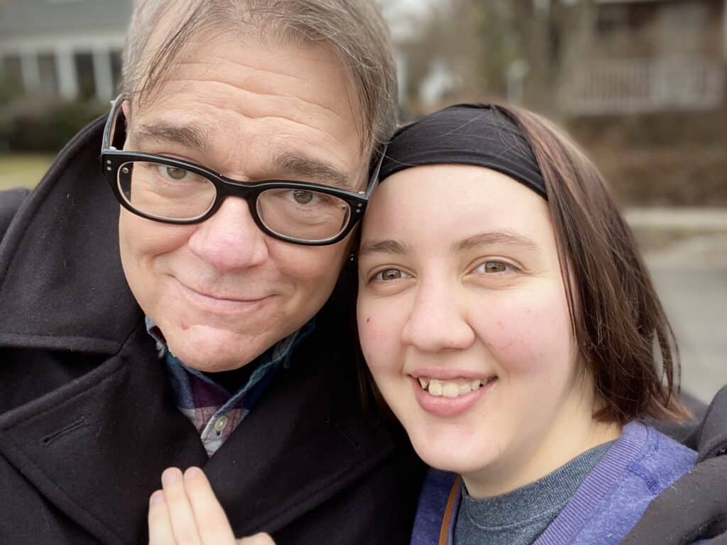 Father (white man) and daughter (white woman) smiling with daughter’s hand on father’s chest