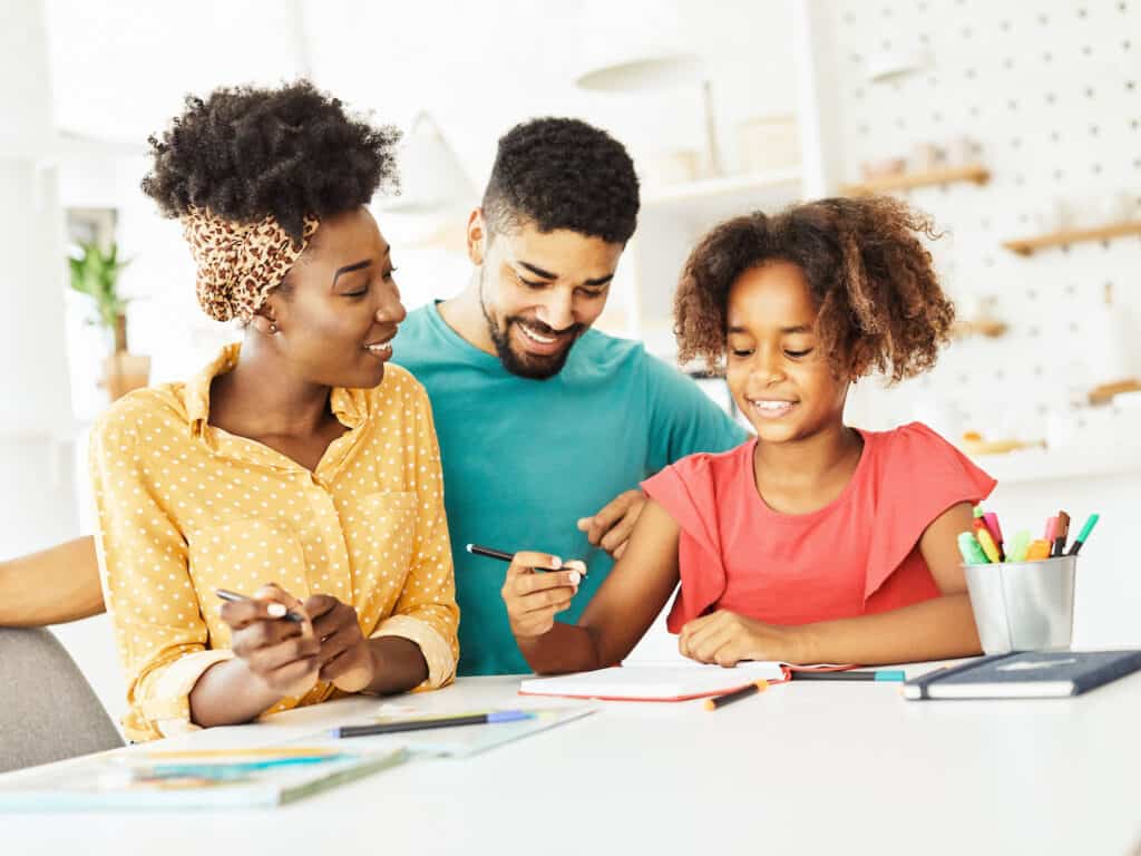 2 adults cooperate with a child to help her complete a school project.