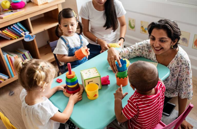 Three children sit at a table playing with their preschool teacher