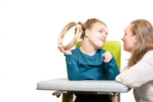 A girl in with cerebral palsey holds a tambourine while she works with her music therapist