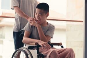A teen in a wheelchair laughs and holds hands with his dad, who has his back