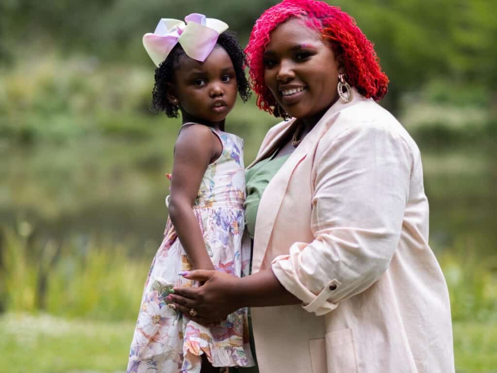 Black mother smiling with her daughter in front of greenery