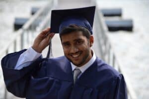 A young man in a cap and gown smiles at his graduation.