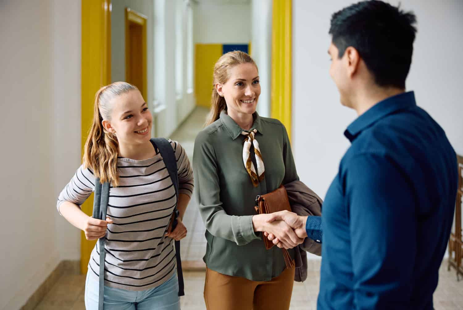 A principal warmly welcomes a student and her mom to school.
