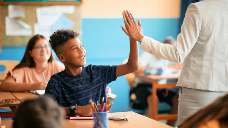 A teacher gives a high five to a smiling student.