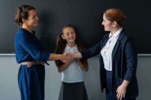 Mom and daughter meet the new teacher with a friendly handshake.