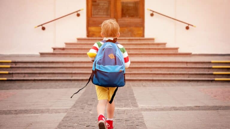 A small child with a backpack heads into a school building.