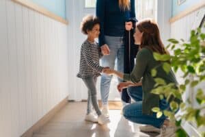 A young girl smiles as her mom introduces her to her new kindergarten teacher.